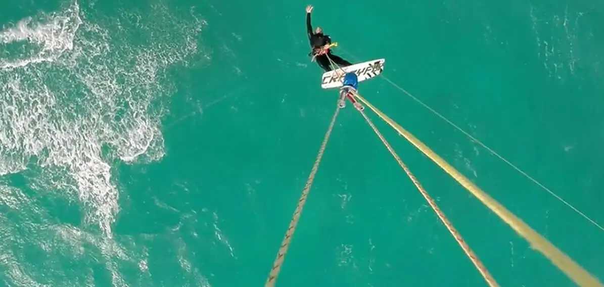 kiteboarding | Greenwood Beach Resort, Cat Island, Bahamas Person kiteboarding over turquoise water, riding a board pulled by long lines from a kite above.